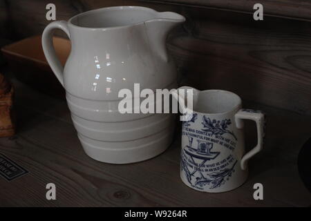 On Set in the Period Style Kitchen - A Victorian Drinking Pitcher and blue & white cream jug on a wooden shelf. Stock Photo