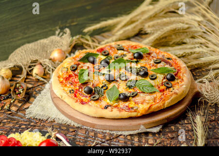 Mixed pizza with chicken, pepper, olives, onion, basil on pizza board. Close up view of baked homemade piza. Rustic pizza home made food. Stock Photo
