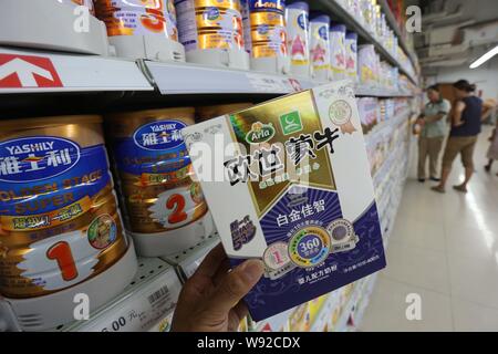 --FILE--A Chinese customer shows a box of Mengniu Arla milk powder in front of tins of Yashily baby milk powder of Guangdong Yashili Group Co., Ltd. a Stock Photo