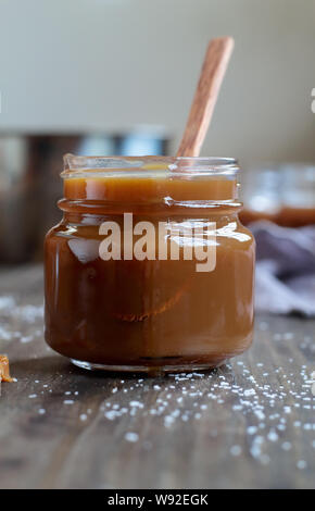 Open jar of salted caramel sauce over a rustic table. Selective focus with blurred background. Stock Photo