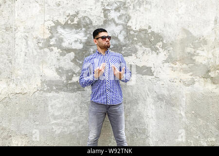 This is me. Portrait of proud handsome bearded young man in checkered blue shirt and sunglasses standing against concrete gray wall. showing himself a Stock Photo