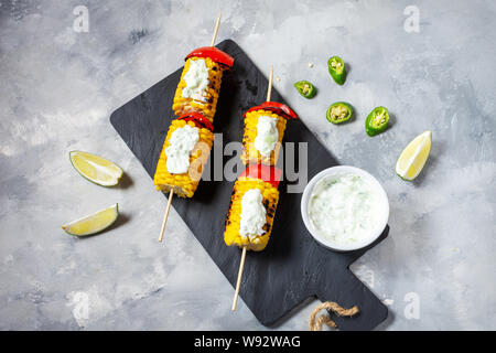 Grilled sweet corn on the sticks, concrete textured table Stock Photo