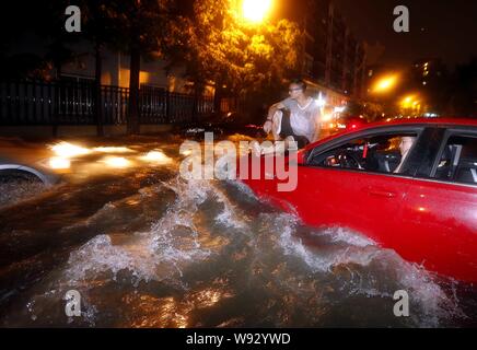 A man sits on a hood of a car on a flooded street after heavy rain hits Hangzhou, east Chinas Zhejiang province, 24 June 2013.   On June 24, 2013 even Stock Photo