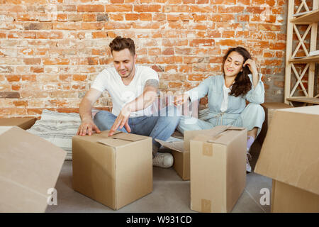 Young couple moved to a new house or apartment. Unpacking cardboard boxes together, having fun at moved day. Look happy, dreamful and confident. Family, moving, relations, first home concept. Stock Photo