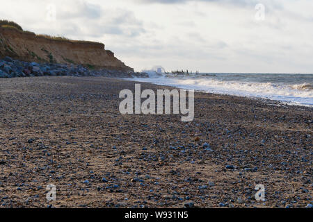 North sea waves break over sea defences protecting the fragils cliffs of Happisburgh beach on a summer evening Stock Photo