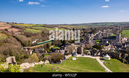 Corfe Castle, England, UK - March 27, 2019: A steam train passes Corfe Castle village on the Swanage Railway in Dorset.