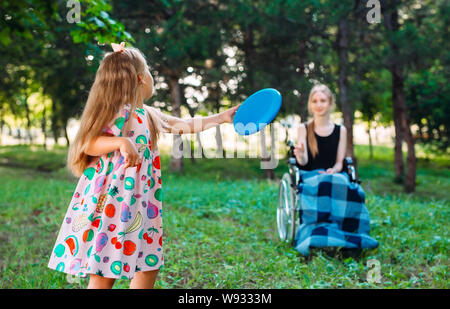 A young disabled girl plays Frisbee with her younger sister. Interaction of a healthy person with a disabled person Stock Photo
