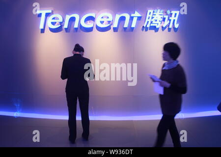 --FILE--A Chinese employee, front, walks past another using her mobile phone in front of a signage of Tencent at its headquarters in Shenzhen city, so Stock Photo