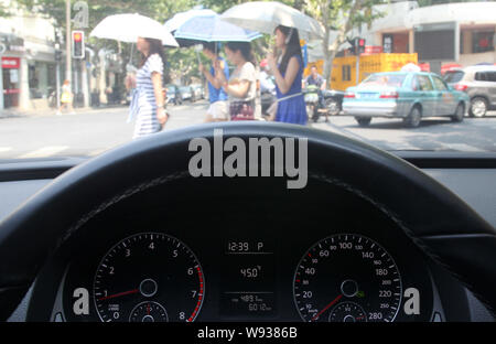 The thermometer in a car shows the current outdoor temperature reaching 45 degrees Celsius as pedestrians shield themselves with umbrellas from the sc Stock Photo