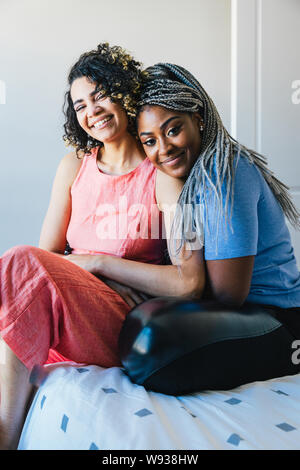 Portrait of happy lesbians sitting on bed at home Stock Photo