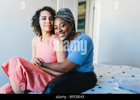Portrait of confident happy lesbians sitting on bed at home Stock Photo