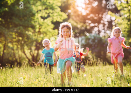 Large group of kids, friends boys and girls running in the park on sunny summer day in casual clothes .