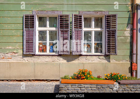 Bunch of dolls staring in Windows with open shutters in state of slight decay Stock Photo