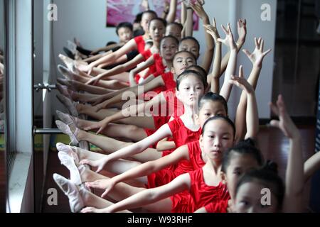 Young Chinese girls bend their bodies and stretch their legs on a ballet barre to learn ballet dancing during summer vacation at a school in Dongxiaon Stock Photo