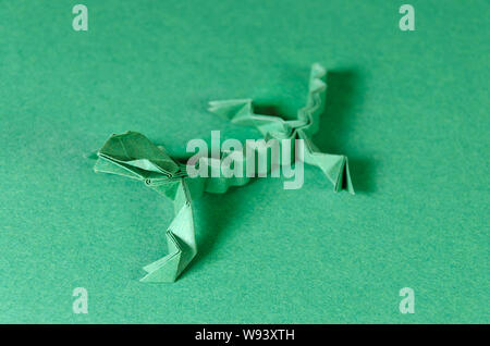 Green origami lizard on green background. Japanese art of paper folding. Flat square sheet of paper transferred into a finished sculpture. Stock Photo