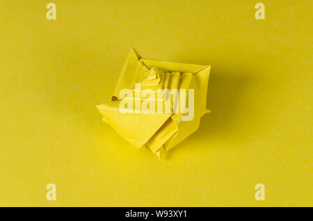 Yellow origami seashell on yellow background. Japanese art of paper folding. Flat square sheet of paper transferred into a finished sculpture. Stock Photo