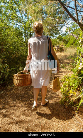 woman in a white dress taking her basket of food to feed the chickens on a small holding Stock Photo