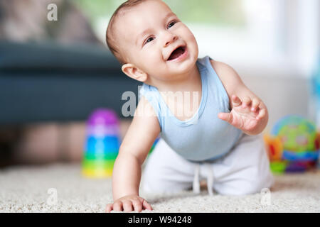 Cute smiling baby boy crawling on floor in living room Stock Photo