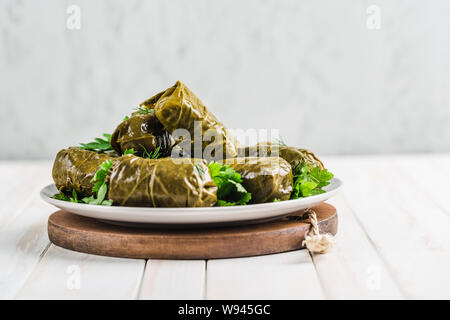 Delicious stuffed grape leaves (traditional doom Mediterranean cuisine Dolma) on a black plate with fresh cilantro and dill on a light wooden backgrou Stock Photo