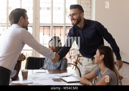 Two happy businessmen shake hands at group negotiation greeting Stock Photo