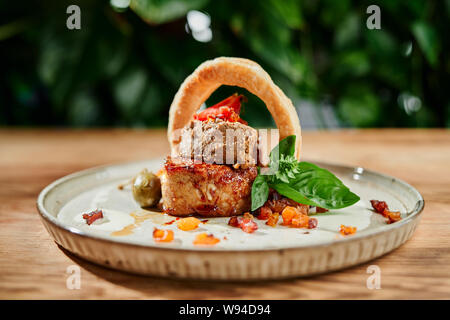 Side view of delicious meal cooked in restaurant. Piece of roasted meat served with breaded squid ring, greaves, mint and olive on plate in cafe. Concept of dinner, food and cuisine. Stock Photo