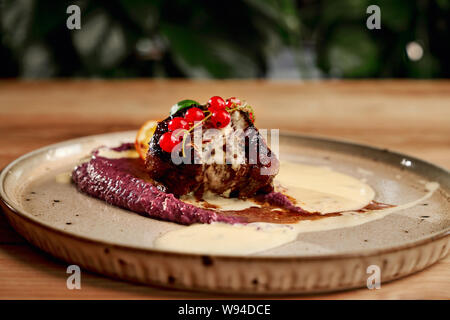 Piece of roasted kebab served with delicious puree, cranberry and lemon. Closeup of tasty grilled meat staying on plate on blurred background. Concept of meal, food and cuisine. Stock Photo
