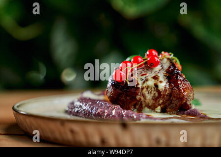 Closeup of tasty juicy piece of kebab with cranberry and vegetable puree staying on plate on blurred background. Delicipus roastet meat in restaurant. Concept of cuisine and food. Stock Photo