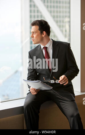 Thoughtful businessman looking through an office building window. Stock Photo
