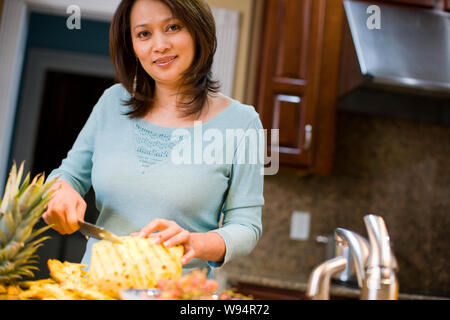 Mid adult woman cutting pineapple in kitchen Stock Photo
