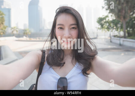 Beautiful asian solo tourist woman taking selfies on a camera in urban city downtown. Vacation travel in summer.