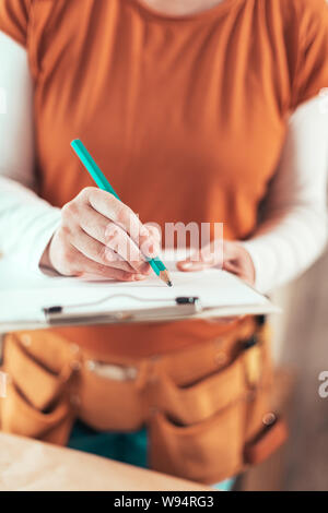 Self employed female carpenter writing project notes on clipboard notepad paper in small business woodwork workshop Stock Photo