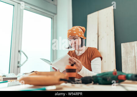 Female carpenter reading DIY project instruction manual in small business woodwork workshop Stock Photo