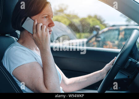 Woman driving car off-road and talking on mobile phone, side view from a passenger seat of adult caucasian female person with smartphone gripping the Stock Photo