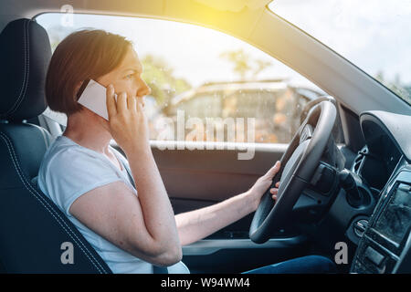 Woman driving car off-road and talking on mobile phone, side view from a passenger seat of adult caucasian female person with smartphone gripping the Stock Photo