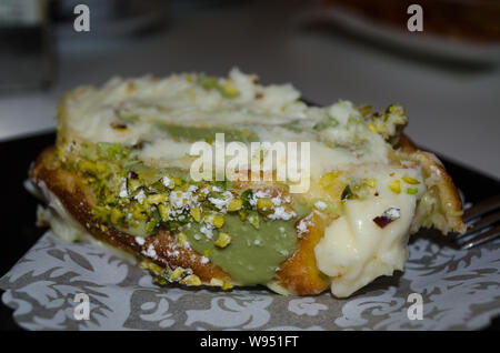 Typical Italian and Sicilian dessert – role pasta di bigne with ricotta and pistachio. Closeup of italian dessert on the plate in the bar. Stock Photo