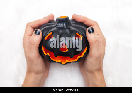 Woman hands with black nail polish holds black carved pumpkin / Haloween concept  background Stock Photo