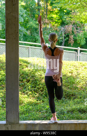 Athletic woman doing warming up exercises stretching her leg muscles before a workout and one arm up Stock Photo