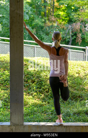 Athletic woman doing warming up exercises stretching her leg muscles before a workout and one arm up Stock Photo