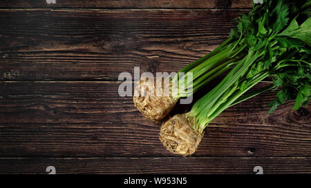 Two fresh celery roots with green leaves on dark wooden board, view from above, space at left side Stock Photo