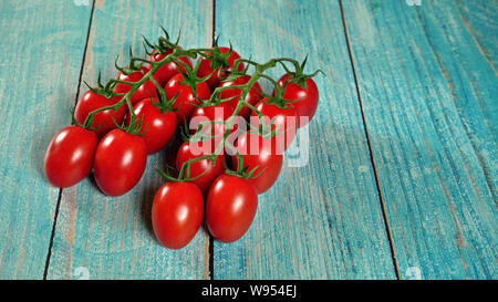 Group of fresh red tomatoes with green stem vines, on wooden boards painted blue, space for text right side