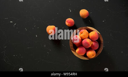 Flat lay photo - apricots in small wooden bowl, on black marble like table, space for text left side Stock Photo