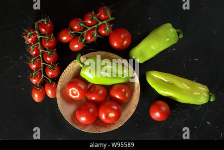 Tomatoes and green bell peppers in small bowl and on black board, view from above Stock Photo