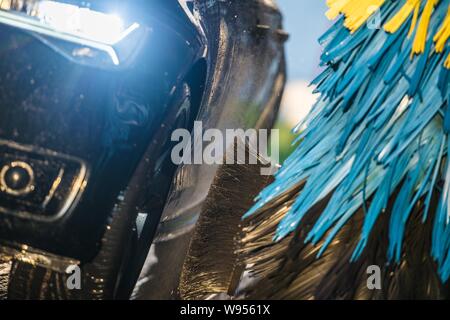 Modern Vehicle in Automatic Car Wash. Closeup Photo. Body and Wheels Washing Brushes Stock Photo