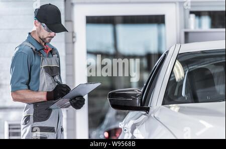 Caucasian Car Service Worker Making Documentation About Vehicle Issues. Car Maintenance In the Authorized Service Center. Stock Photo