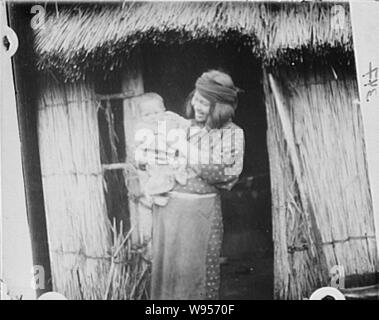 Ainu woman holding a child standing outside a hut Stock Photo