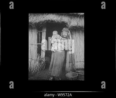 Ainu woman holding a child standing outside a hut Stock Photo