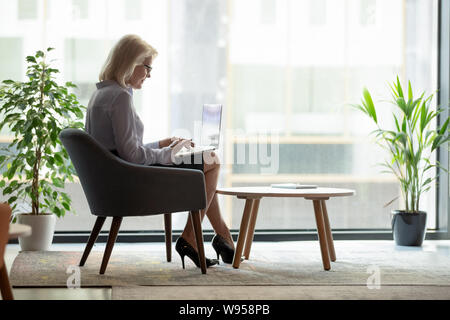 Successful mature businesswoman using laptop near big window Stock Photo