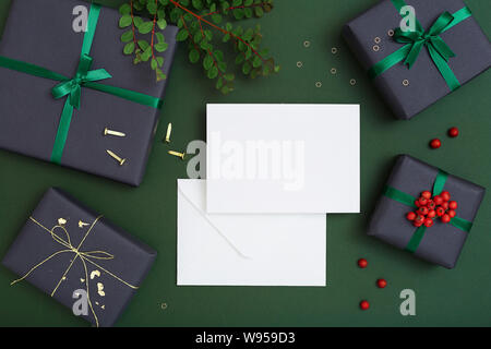 Christmas greeting card blank mockup, postcard template flat lay on green background with gift boxes Stock Photo