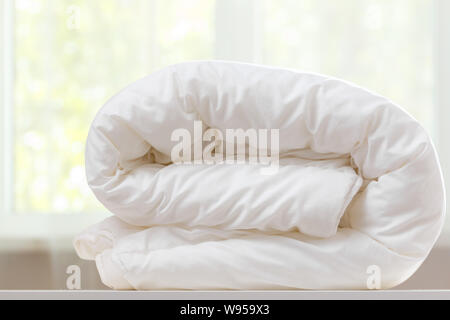 A folded white duvet lies on a table on a blurred background. Stock Photo