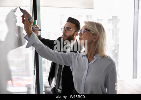 Mature businesswoman training employee, drawing on flip chart Stock Photo